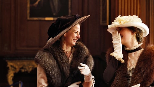Two women wearing Regency clothes look at each other and laugh whilst exploring the house at Lyme, Cheshire.